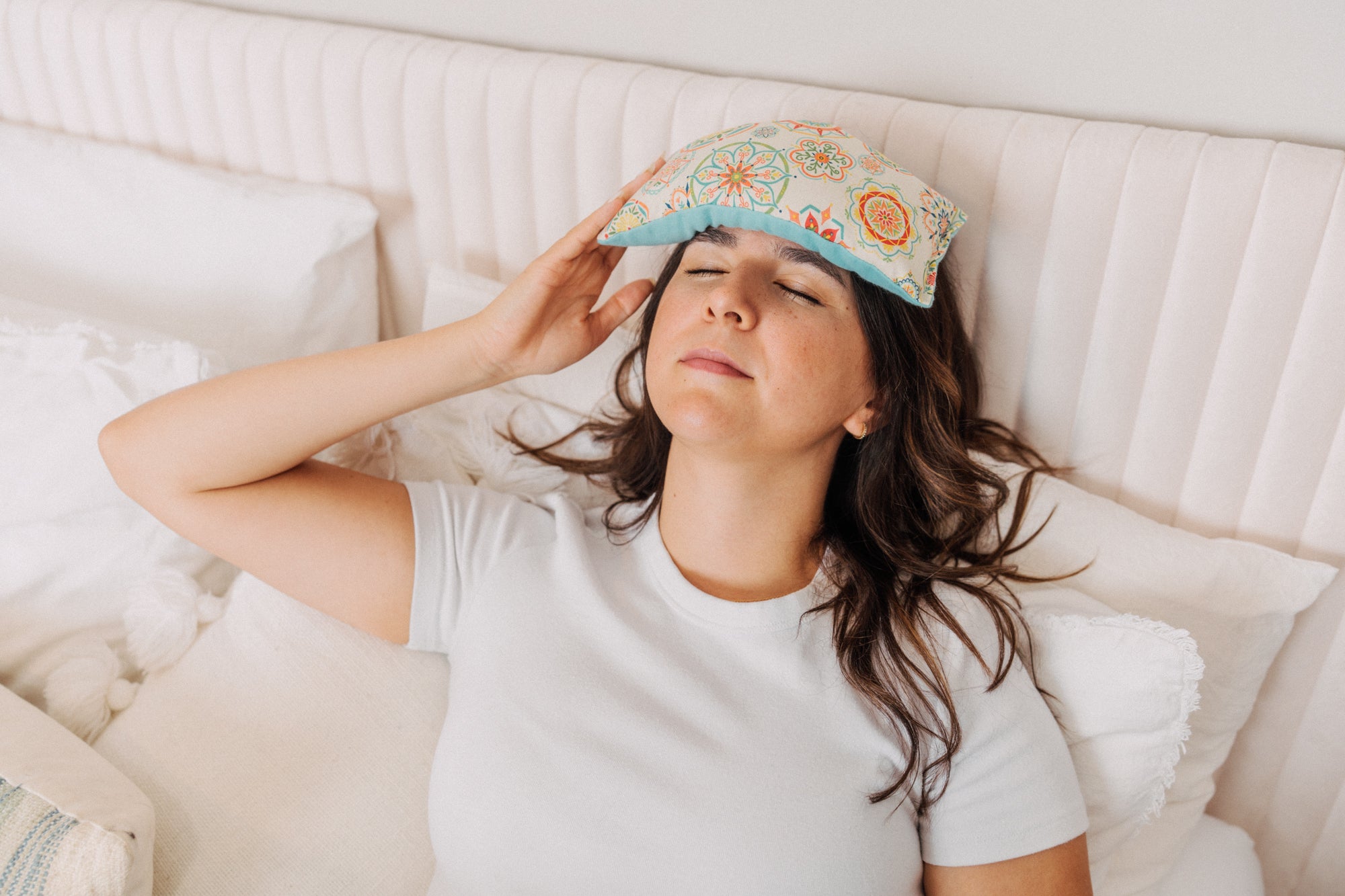 lady with cream medallion eye pillow covering forehead to soothe a headache 